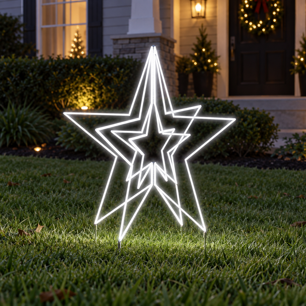 A large white LED star yard light with nested star shapes stands on a green lawn in front of a house at night, casting a bright glow on the grass.